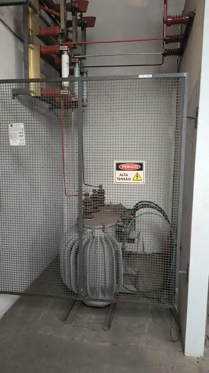 Transformador de cabine primária atrás da grade de proteção, com placa de alta tensão