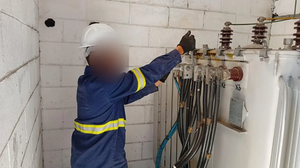 Eletricista com capacete e uniforme refletivo ajustando as conexões do transformador