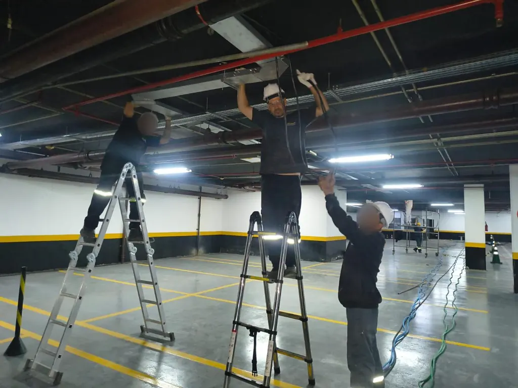 Equipe em escadas instalando infraestrutura elétrica no teto de uma garagem