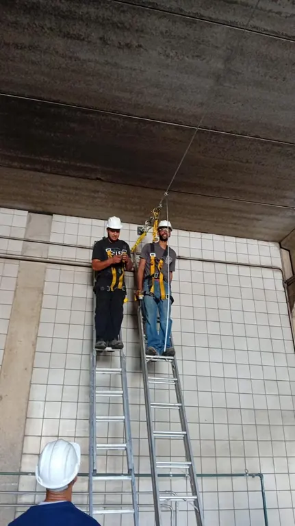Dois técnicos com cinto de segurança em escadas sob a cobertura
