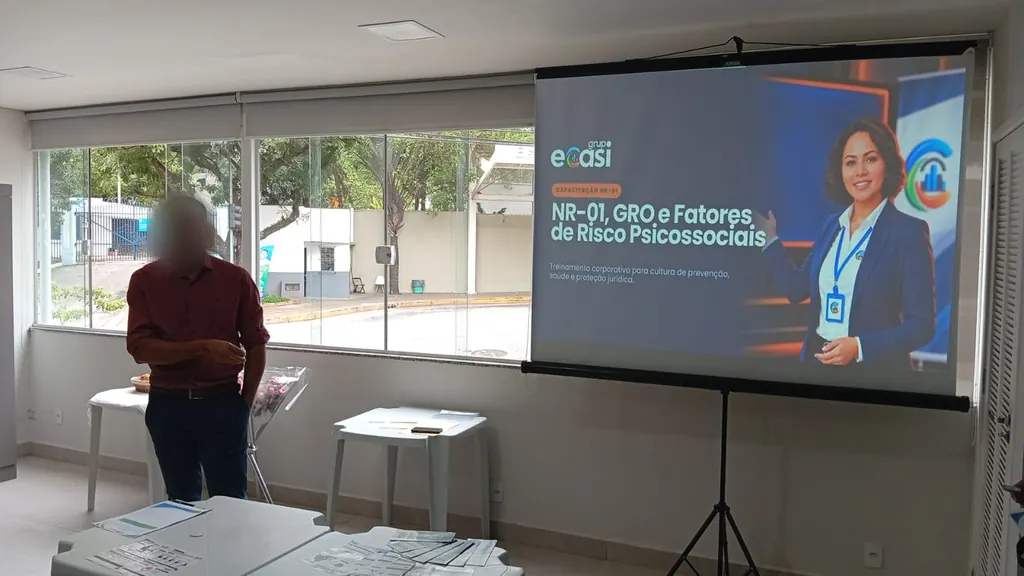 Instrutor ao lado da projeção do treinamento de NR-01, GRO e fatores de risco psicossociais